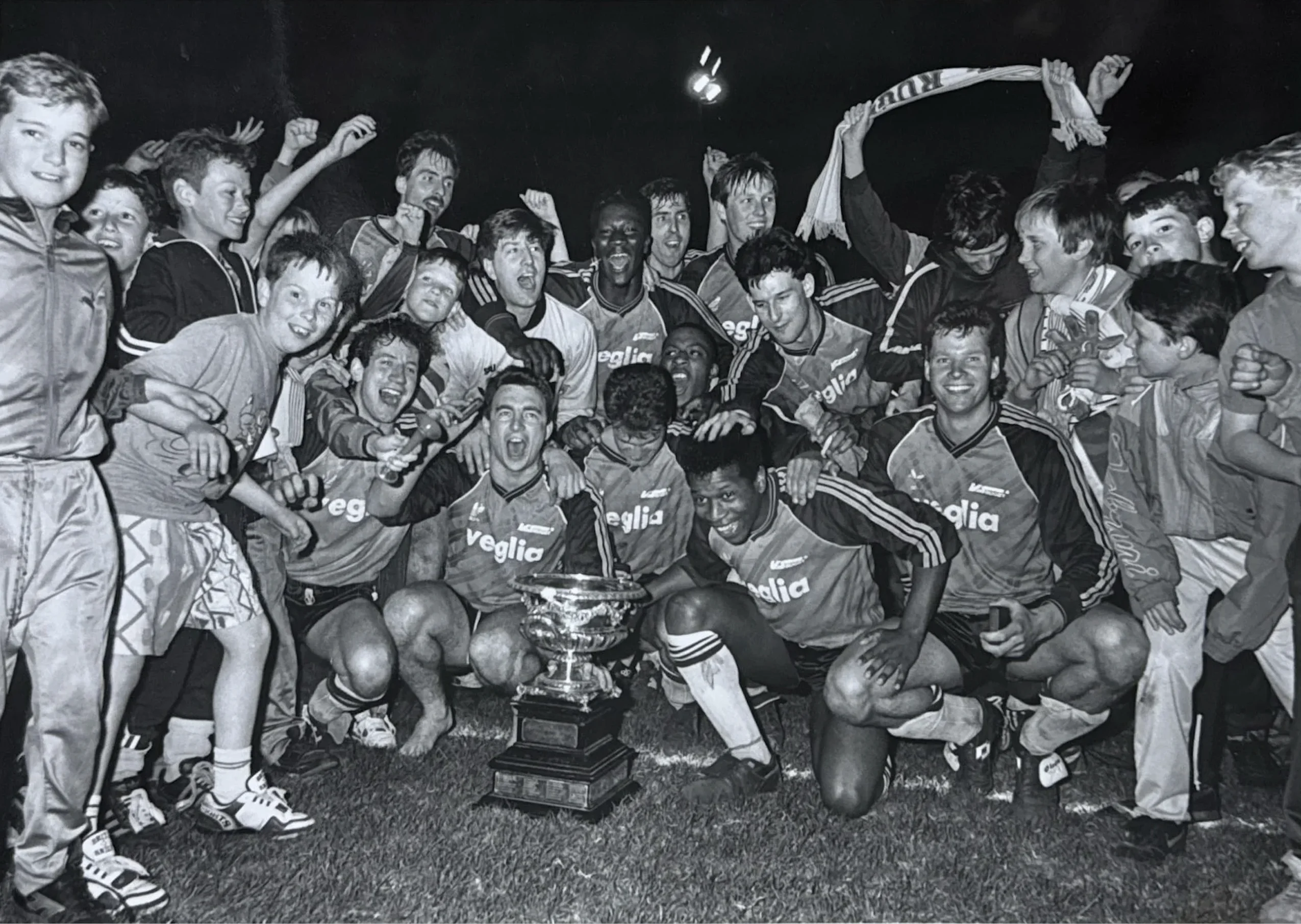 VS Rugby players celebrate with the trophy, mobbed by supporters on the pitch