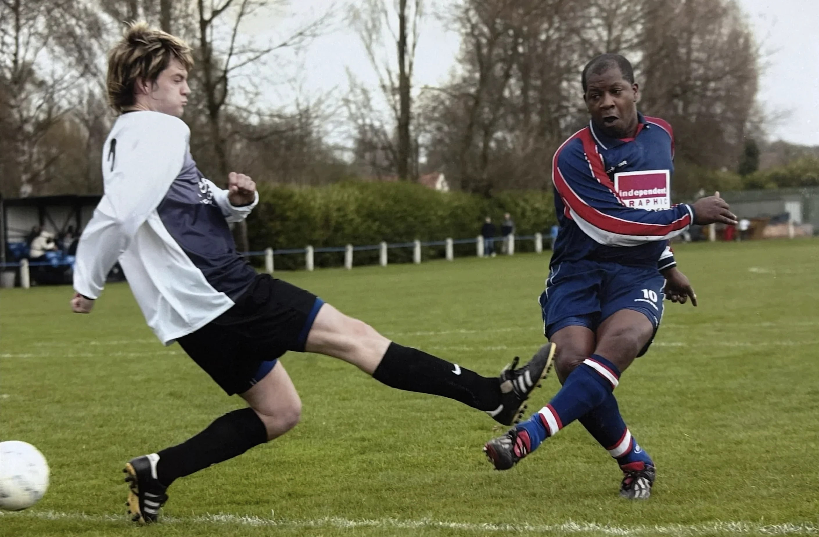 Mark Rosegreen in action in a blue and red strip, shooting past a sliding defender
